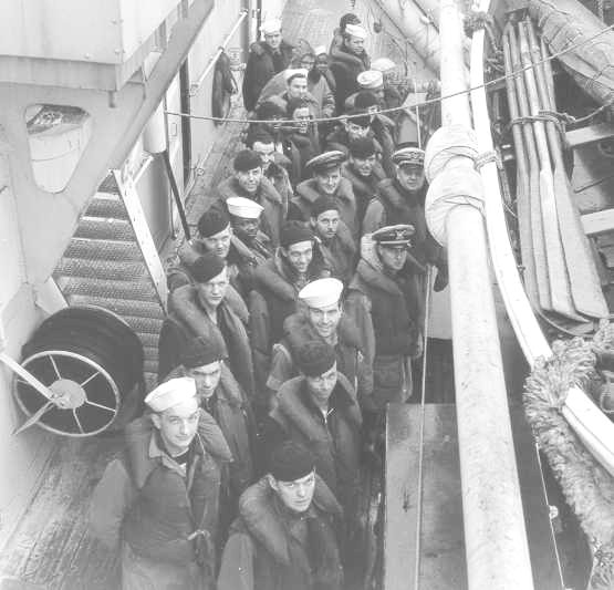 Approximately 25 uniformed sailors are standing close together and looking toward the photographer.